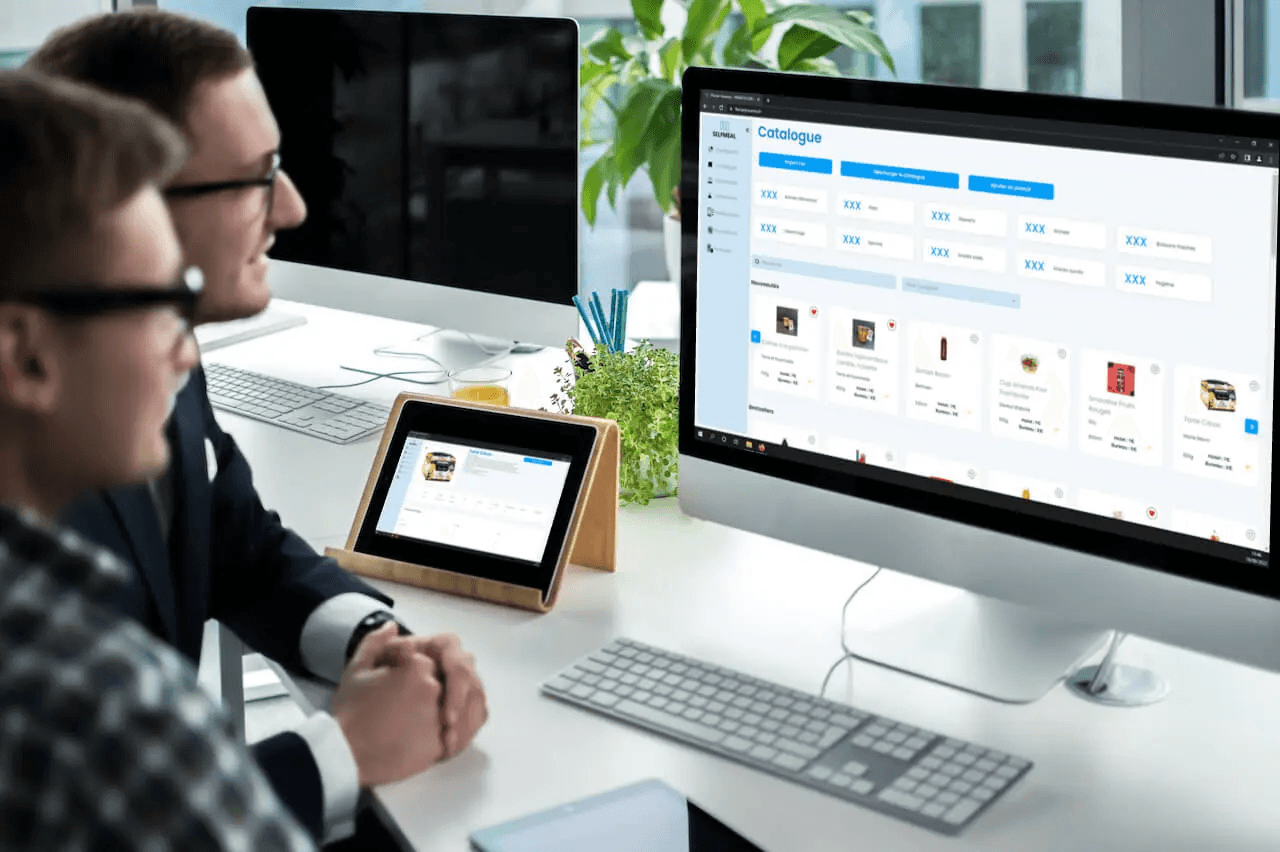 Équipe échangeant devant un catalogue web affiché sur ordinateur et tablette